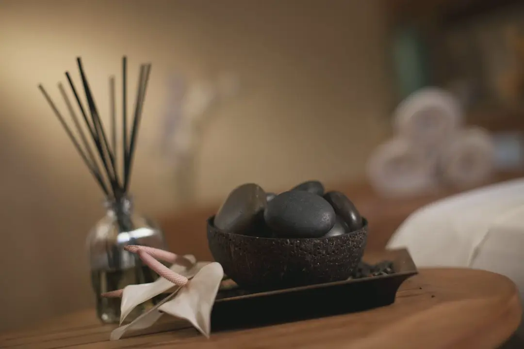 A bowl of smooth dark stones and a reed diffuser on a treatment-room table